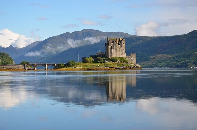 Eilean Donan Castle reflected in a flat-calm loch, mist on the hills behind