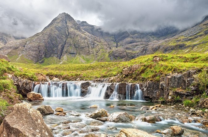 One of the Fairy Pools waterfalls in a green glen, the dark peaks of the Black Cuillin rising behind