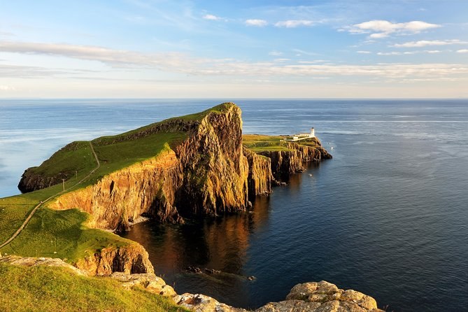 Neist Point in low evening sun, the headland's cliffs glowing gold and the lighthouse at its far end above a calm sea