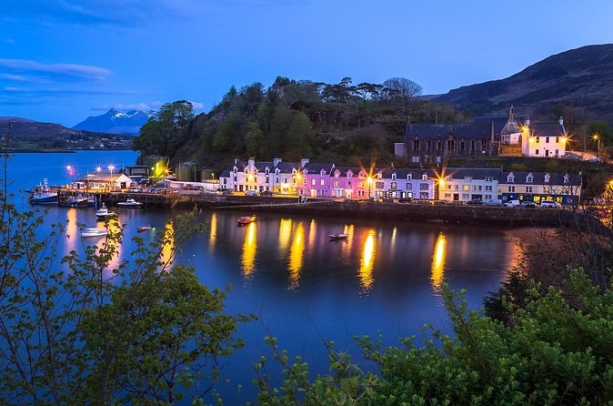 Portree harbour at night, the painted houses lit along the quay and their lights on the water