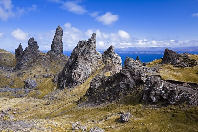 The Storr's rock pinnacles close up, standing out of a field of fallen boulders and grass, the sea on the horizon