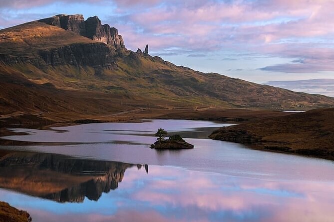 The Storr ridge at dusk, the Old Man a small spike at its end, reflected pink and brown in a loch with one wooded islet